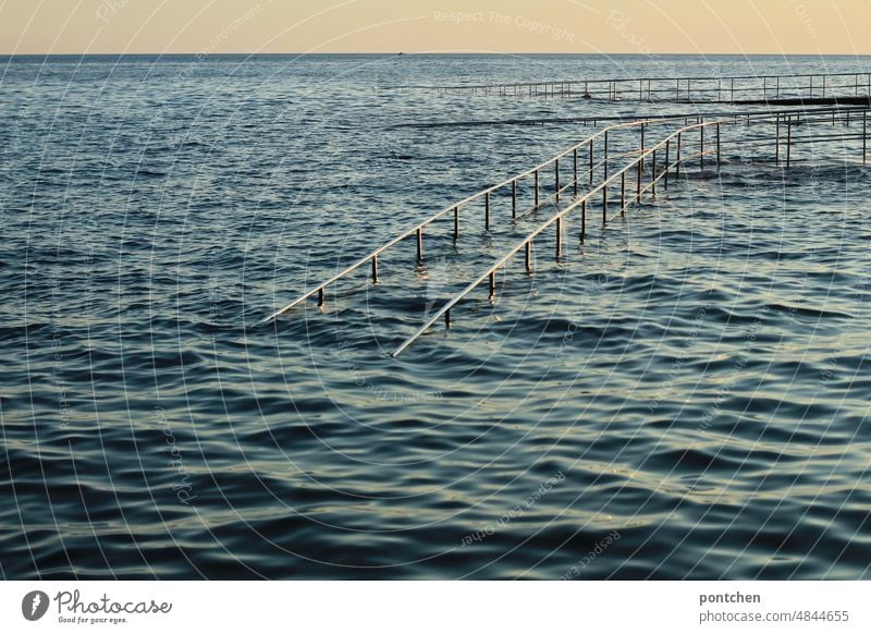 A flooded footbridge with metal railing leads into the sea. Evening sun, sunset on the sea Water Ocean Waves Footbridge evening light Sunset inundation
