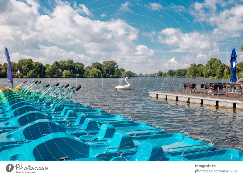 Colorful pedal boats next to wooden jetty on lake. Group of colorful pedal boats next to wooden pier of lake. Swan pedal boat on lake Aasee in Münster, Germany.