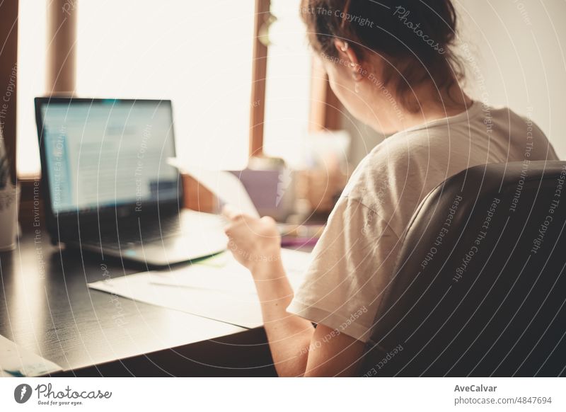 Back image of a young woman studying and working on his home desk, doing homework during university and freelancer activities working from home concept. person