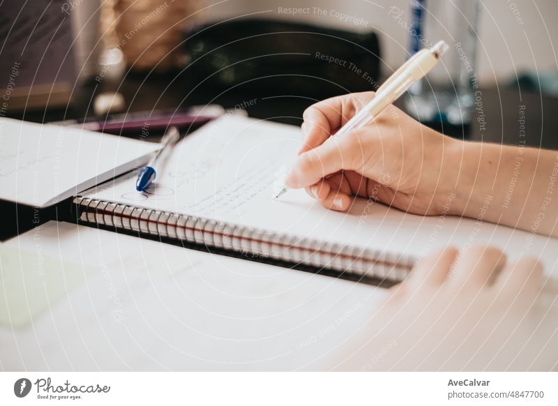 Closeup image of a woman hand writing on a notebook, doing homework during university, preparing for exam with textbook and taking notes, selective focus on the pencil.