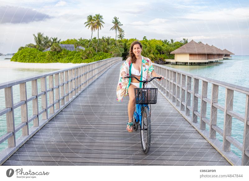 Middle aged woman on a bike crossing a bridge on a Maldive island asian attractive beach bicycle coast coastline exotic female foliage happy holiday landscape