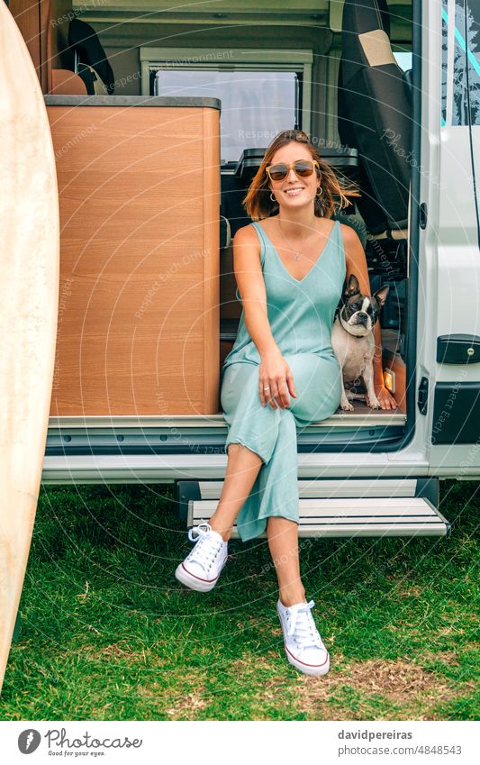 Woman sitting with her dog at the door of her camper van during a trip smiling young woman boston terrier looking camera pet vacation person lifestyle journey