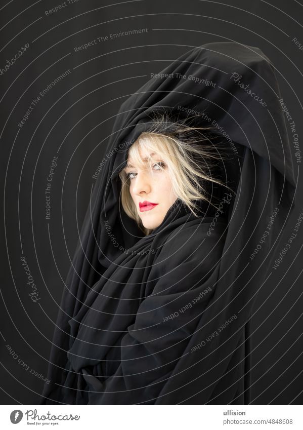 proud blonde fashion beauty model woman, with red mouth and black fabric, cloth with hair electrostatic charged, sticking to cape, against black background