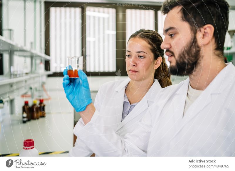 Chemists examining chemical liquid in lab scientist colleague laboratory chemist sample research beaker examine test coworker science focus glove professional