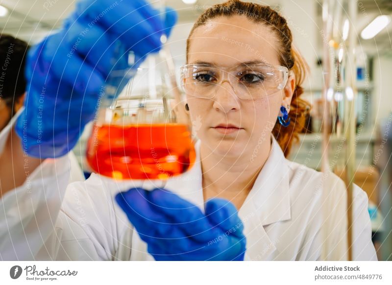 Serious chemist examining liquid in flask in lab woman scientist examine laboratory scientific chemical experiment sample test research expertise science focus