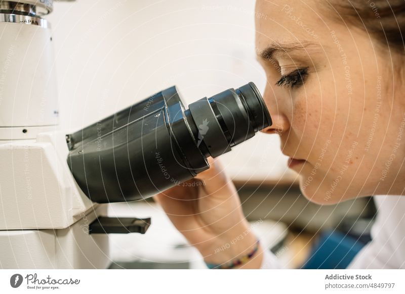 Focused scientist looking through microscope in lab woman examine chemist laboratory research analyze scientific experiment expertise science focus work