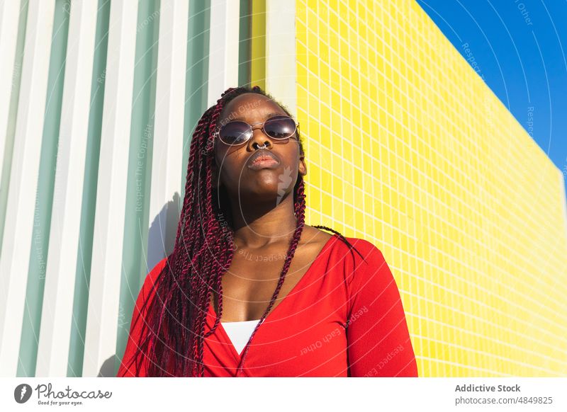 Black woman in trendy outfit and sunglasses portrait leaning style female african american hairstyle sunny modern confident fashion red urban yellow background