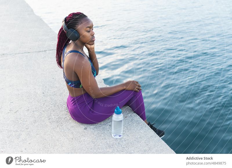 Relaxed black woman listening to music headphones concentration training sportswoman fitness workout female athlete wireless device city gadget outdoors