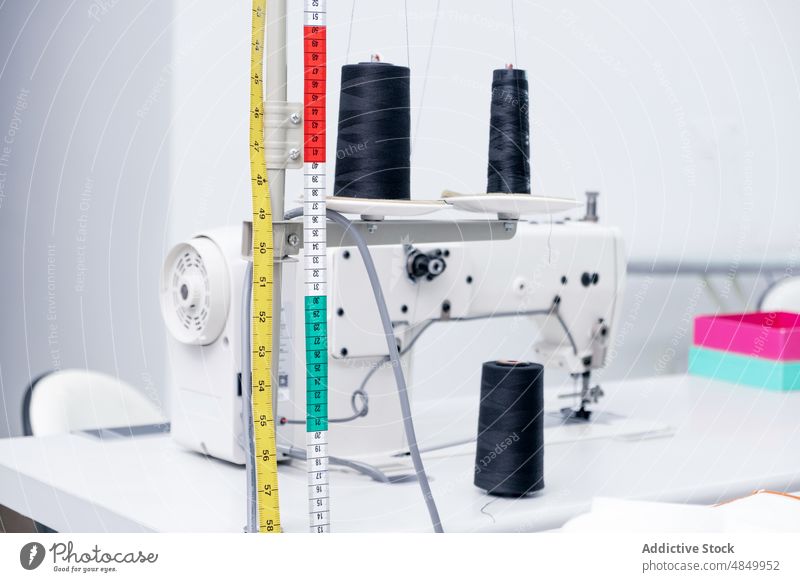 Measuring tape near thread spools on sewing machine measuring supply workshop tool atelier equipment craft yarn design handicraft studio colorful centimeter