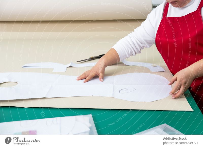 Unrecognizable seamstress working with paper patterns in studio textile atelier workshop fabric dressmaker supply manufacture industry appliance coworker cloth
