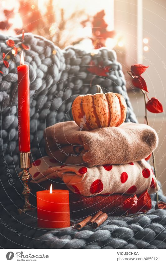 Cozy autumn still life with stapled knitted wool sweaters, candle, pumpkin and branches at grey blanket. cozy warm clothes cold days front view autumn clothes