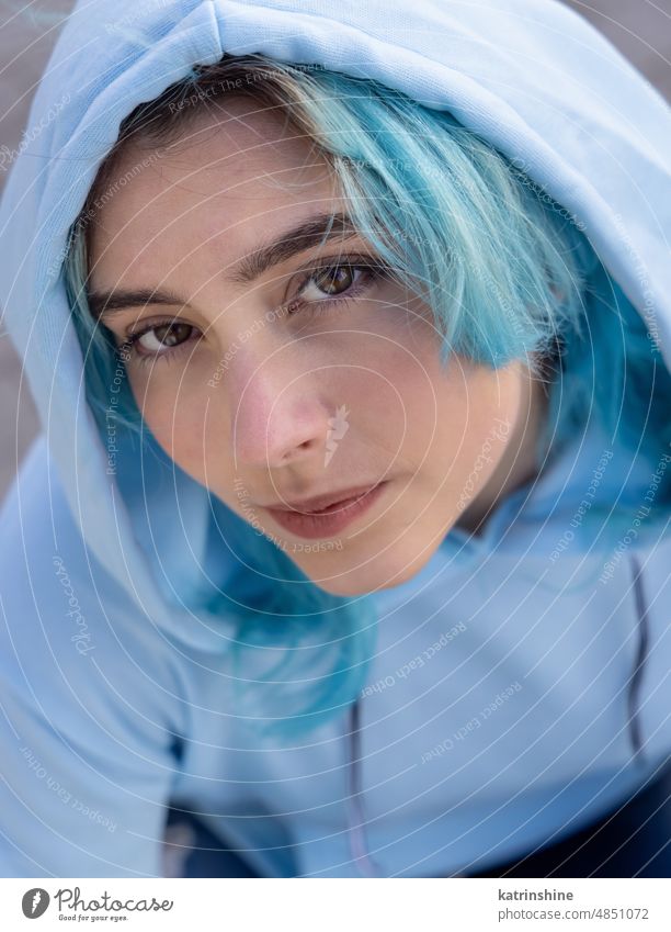 Blue haired Teenage girl in light blue oversize hoodie lookinginto a camera from down Teenager mockup jeans sitting blue haired haunches teen girl outdoors