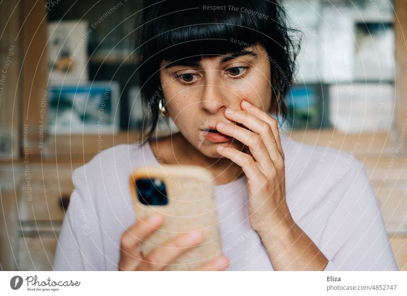 Young woman looks at her smartphone and is shocked Shock bad news Frightening Distress Fear Panic Horror Woman Cellphone Scare stock market crash portrait Bad