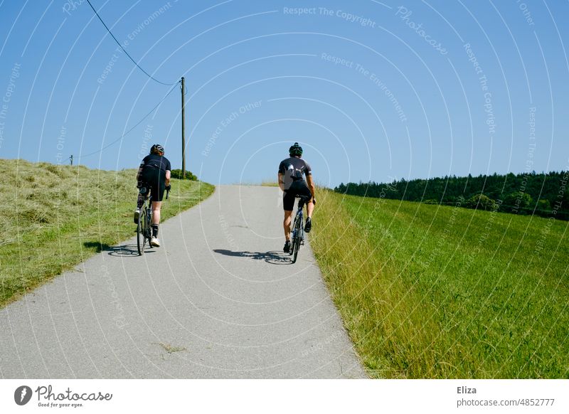 Two sporty cyclists on a bike ride in the countryside Cycling Cycling tour cycling Athletic Green Hill uphill Summer sunshine Exterior shot Sports Bicycle