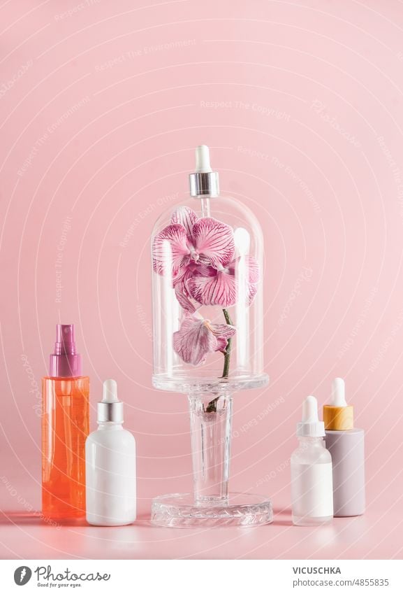 Cosmetic bottles with orchid flowers in bell jar at pale pink background. cosmetic bottles facial treatment concept various skin care beauty products front view