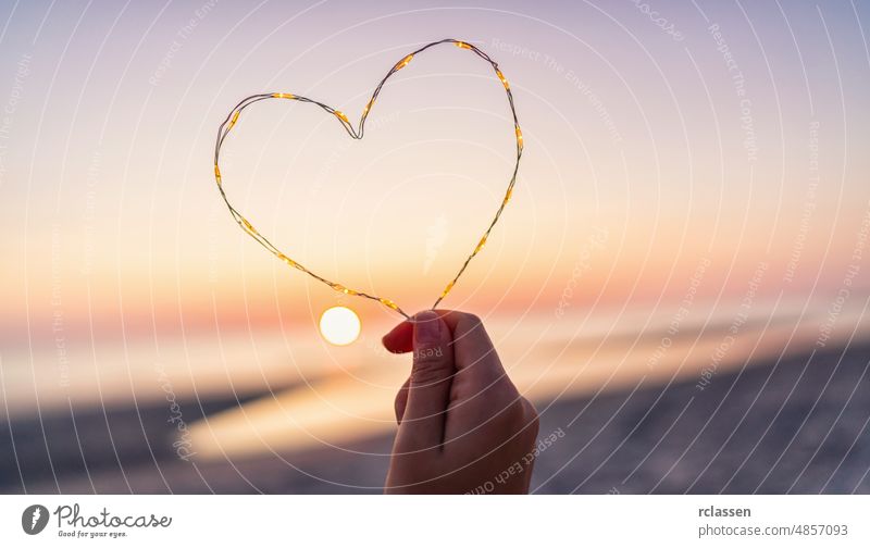 womand holding Heart shape made of led lights at the beach on sunset heart love hand background copy space summer abstract sea holiday beautiful celebration
