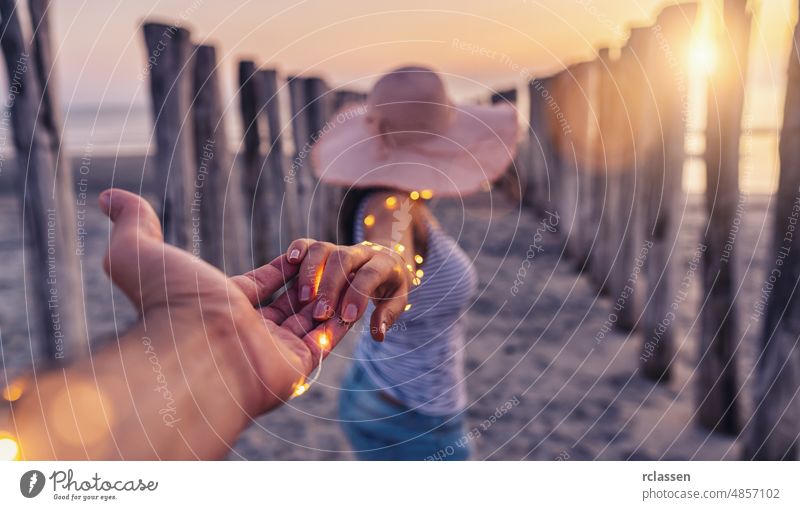 Couple holding hands and walking on beach in sunset, woman with white shirt and shorts jeans couple summer travel sea baltic dune sandy led light bokeh