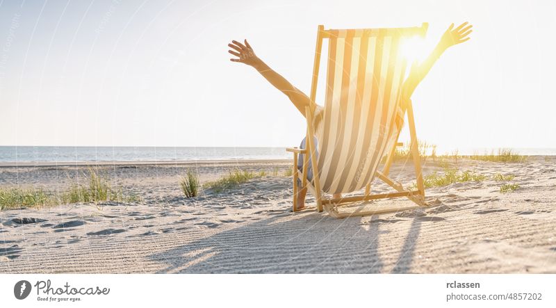 happy young woman sitting on beach chair on beach at summer, copyspace for your individual text, banner size happiness feeling sunset sunlight warm baltic sea