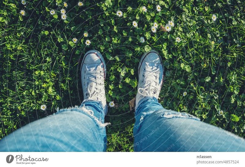 young woman stands in sneakers in a Daisy meadow at spring, high angle footsie or flortrait, personal pespective from above. pov people lifestyle point view way