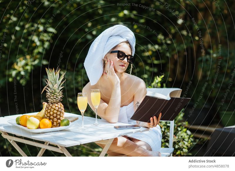 Woman in towels reading book on terrace woman morning patio literature bookworm hobby pastime leisure juice beverage drink feminine summer glass table female