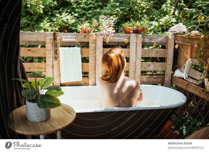Unrecognizable woman sitting in bathtub water patio skin care terrace wellbeing routine topless chill style appearance redhead rest wash summer charming lady