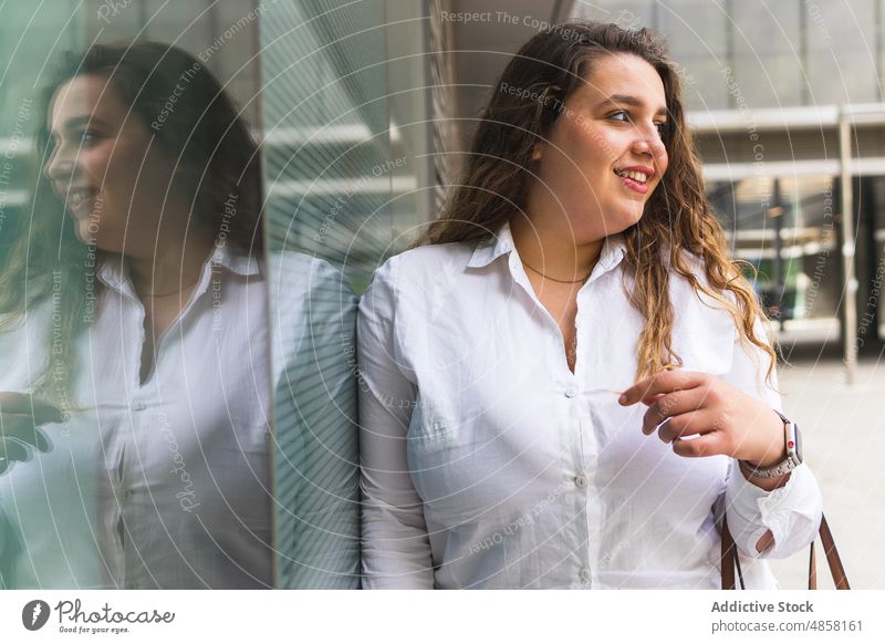 Content woman standing near glass building glass wall street city appearance style urban feminine dreamy reflection female house glad construction content