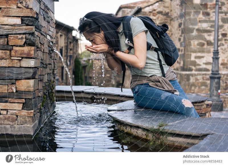 Traveling Asian woman drinking water from fountain travel old town tourism thirst tourist journey hydrate street explorer valverde de los arroyos