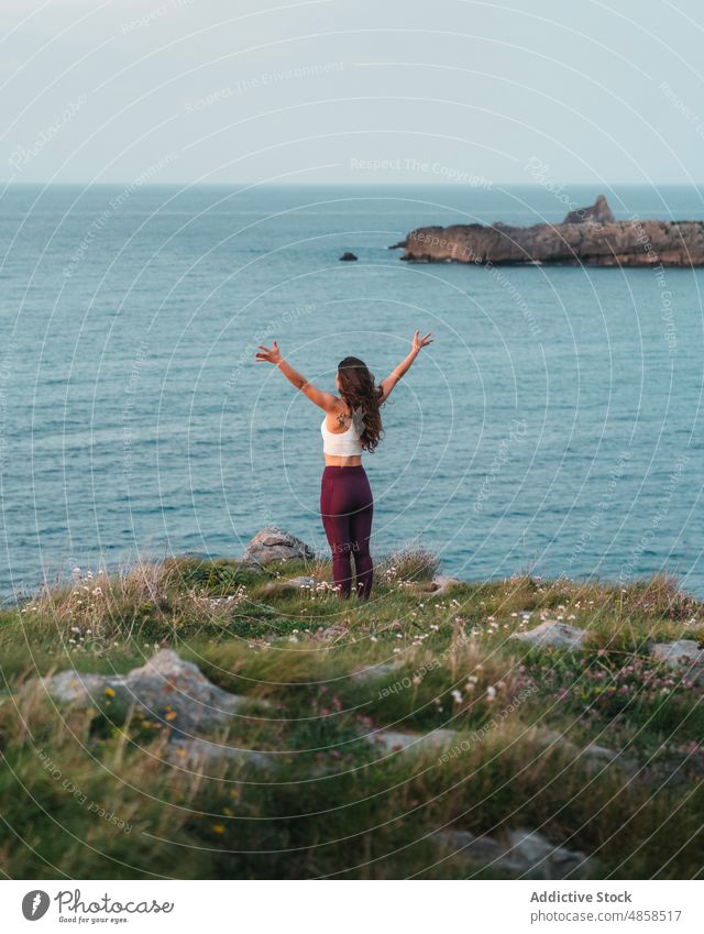 Anonymous woman doing yoga on cliff in front of wavy sea outstretch admire practice wellness freedom wellbeing zen mindfulness nature carefree stress relief