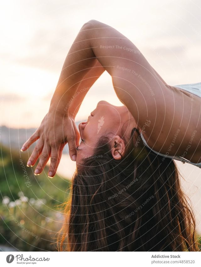 Peaceful woman performing backbend with namaste gesture during yoga session in nature eyes closed wellbeing asana sunset sea practice stress relief wellness