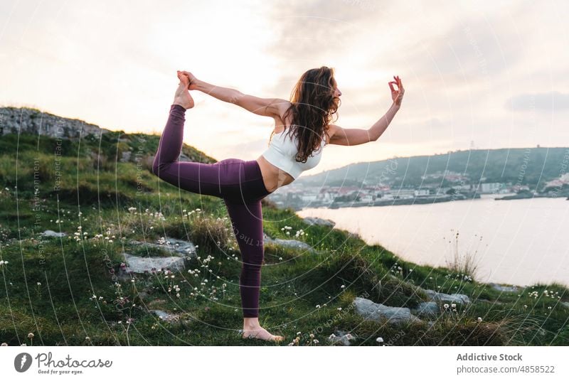 Barefooted lady performing Standing Bow asana on rocky hill woman yoga balance standing bow mountain stretch dandayamana dhanurasana wellness concentrate mudra
