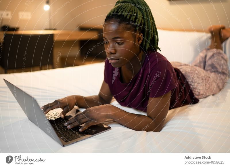 Black woman using laptop on bed browsing netbook work remote bedroom freelance online modern busy female ethnic black african american at home distance gadget