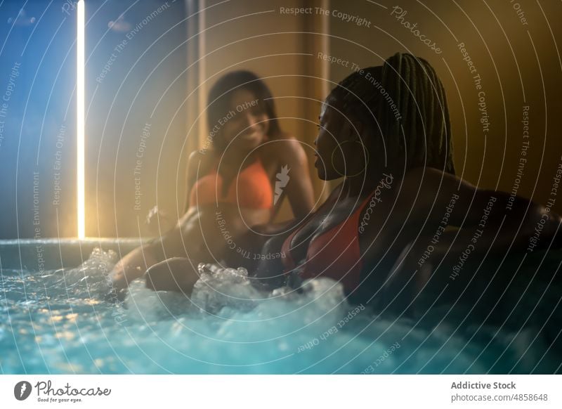 Black women sitting in hot tub friend spa water wellbeing procedure skin care body care chill trendy feminine wellness female african american bikini swimsuit