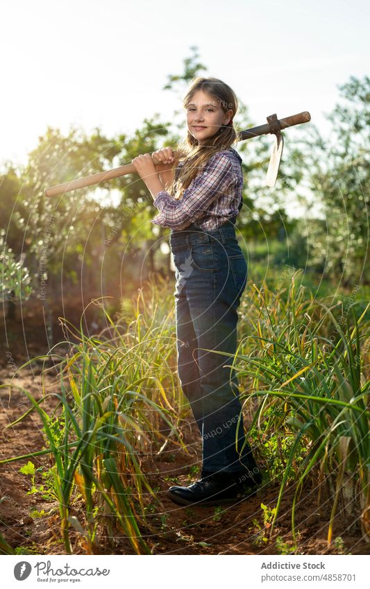 Positive little farmer with hoe girl summer countryside agriculture work scallion portrait carry casual rural child kid sunlight plantation daytime jeans