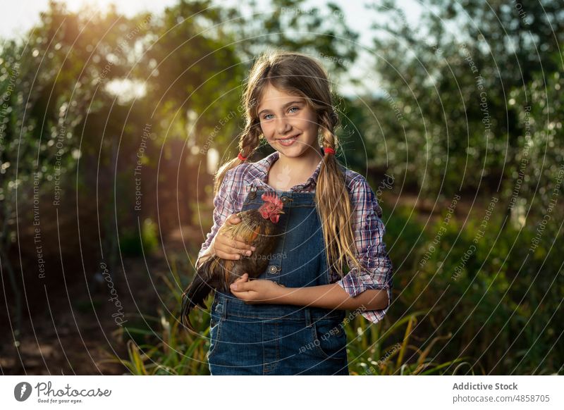 Friendly little farmer with cock girl rooster countryside smile summer animal positive portrait daytime kid casual cheerful happy rural cute adorable nature