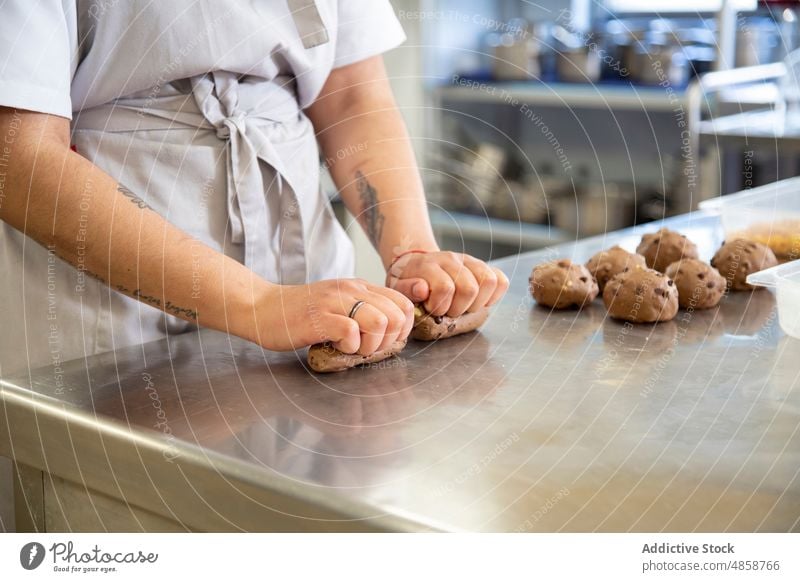 Anonymous woman preparing dough for cookies bakery sweet dessert learn pastry raw unbaked divide culinary school kitchen prepare process industry knead apron