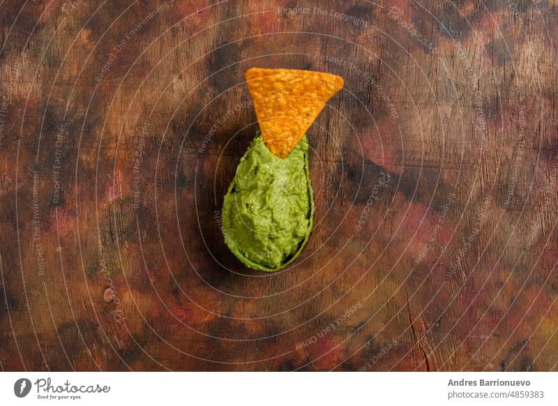 Half an empty avocado filled with guacamole with a triangle of crunchy corn on top on a background in brown tones. Top view. traditional mexican tortilla