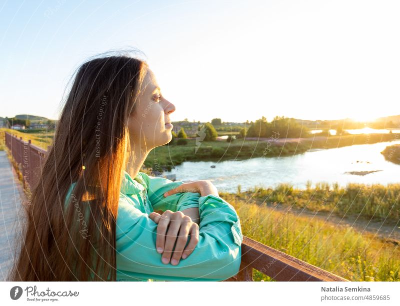 Young girl with loose long hair admiring sunset on river on summer evening in countryside. young girl dreamy golden hour staycation relax wellness mental health