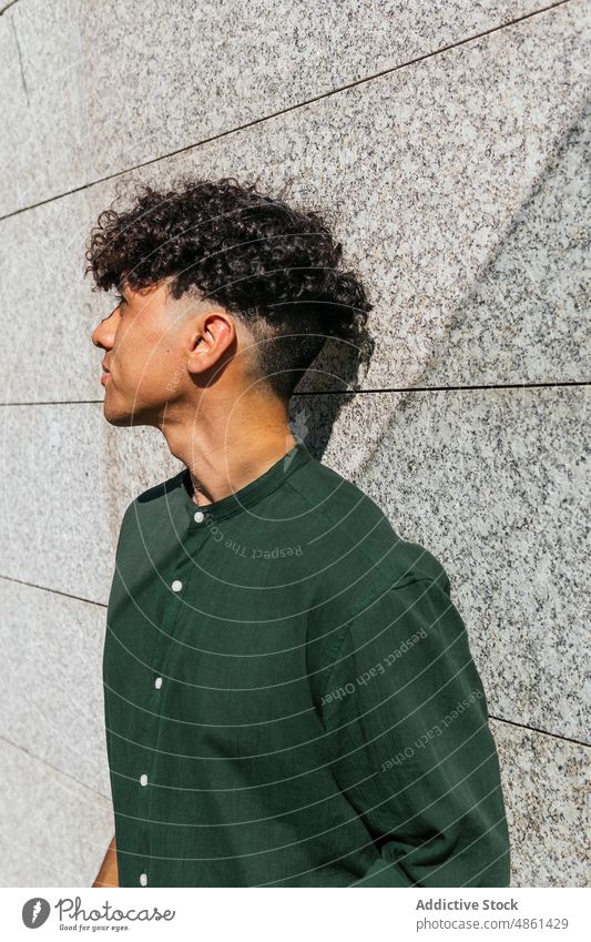 Young stylish man on street style model trendy lean on stone wall gaze city modern male ethnic afro curly hair shirt cool urban daytime sunlight marble stand