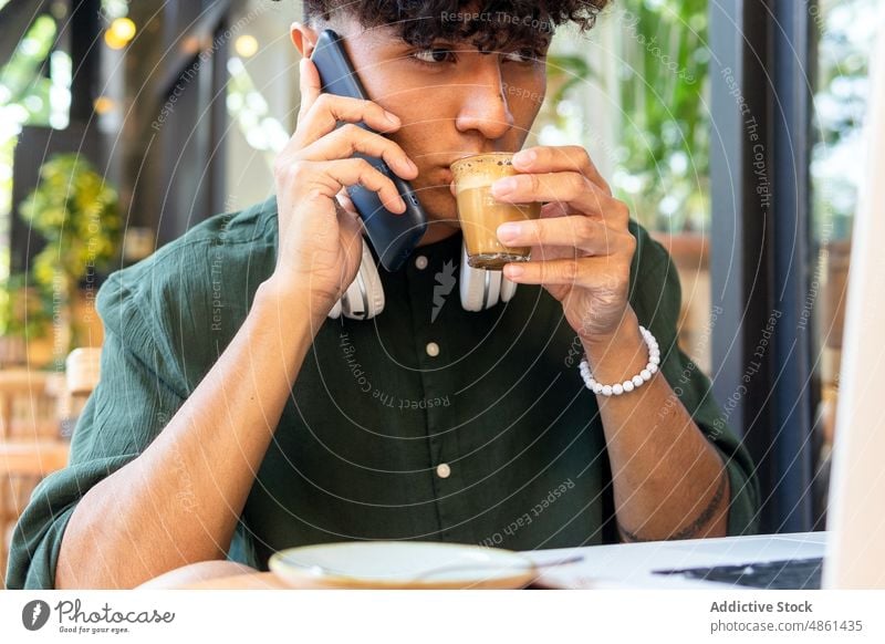 Young man with laptop and smartphone in cafe freelance drink coffee mobile work remote modern netbook device headphones ethnic casual male beverage internet