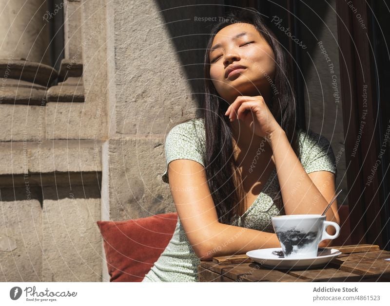 Charming Asian woman at table with coffee in street cafe beverage terrace enjoy dreamy eyes closed summer hot drink feminine coffee break charming cup asian