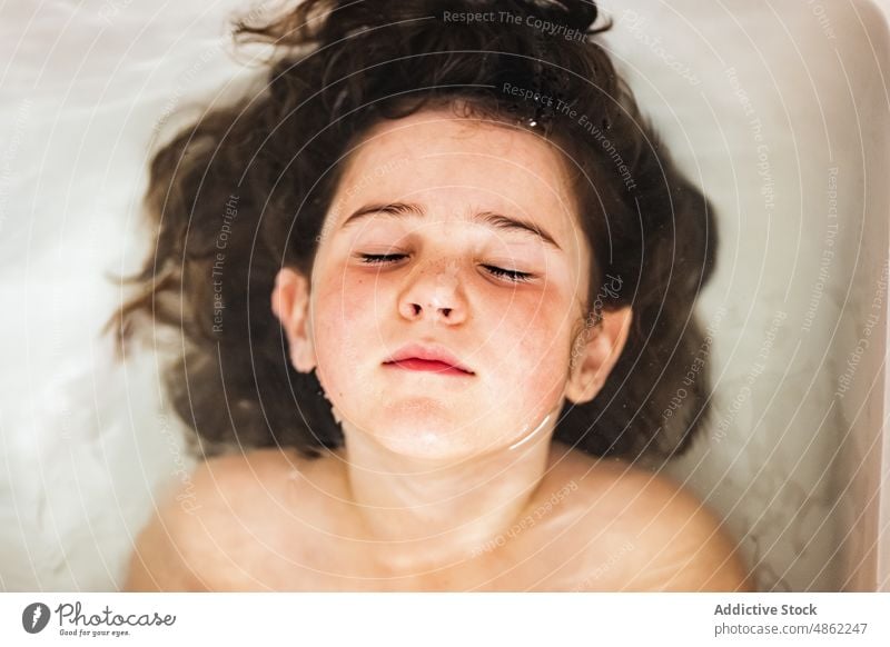 Girl relaxing while bathing at home girl carefree child eyes closed bathtub rest bathroom portrait kid chill lying wet hair water calm serene peaceful hygiene