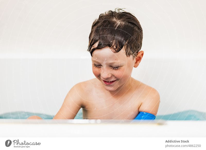 Boy wearing waterproof arm plaster protection in bathtub boy laugh child having fun bathroom white modern play carefree at home smile toothy smile happy