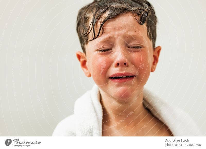 Sad boy with tears on face wrapped in white towel sad upset child eyes closed wet hair cry portrait problem kid unhappy depress frustrate expressive despair