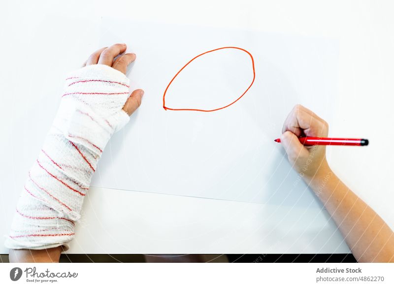 Anonymous boy with broken arm drawing picture marker creative hobby home table kid child sit art pen talent circle hands childhood imagination lifestyle sketch