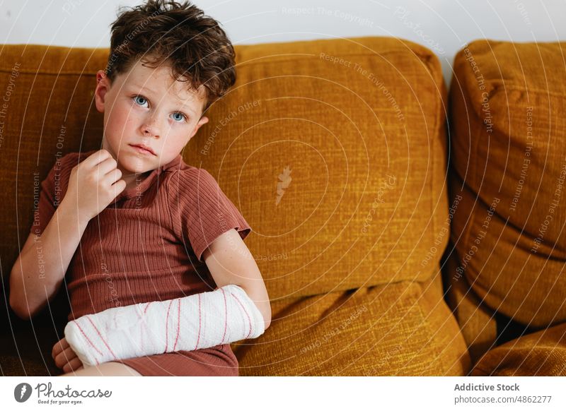 Cute boy with broken arm on couch rest sofa home injury weekend living room portrait bandage plaster touch face kid cute child relax adorable childhood sit