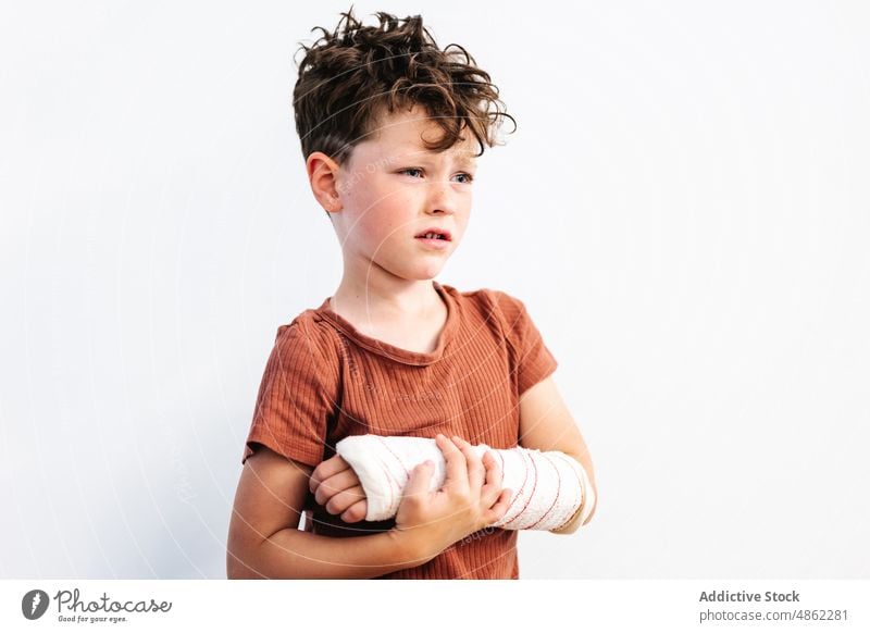 Unhappy boy with broken arm in plaster bandage upset injury patient pain hurt hold frustrate unhappy discomfort problem distress childhood kid protect cute