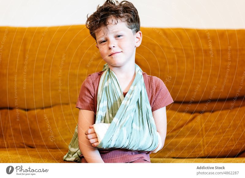 Cute boy with broken arm on couch rest sofa home sling injury weekend living room portrait bandage plaster kid cute child relax adorable childhood sit trauma