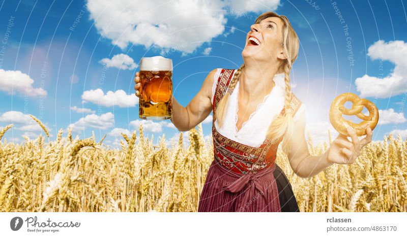 sexy traditional Oktoberfest visitor standing in a wheat field, wearing a traditional Bavarian dress and holding big beer mug and pretzel at autumn in germany
