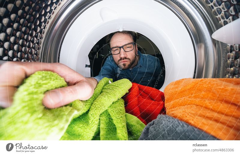Man with glasses reaching Inside a washing machine or dryer doing laundry View from the inside tumble appliance man male caucasian chore clothes clothing