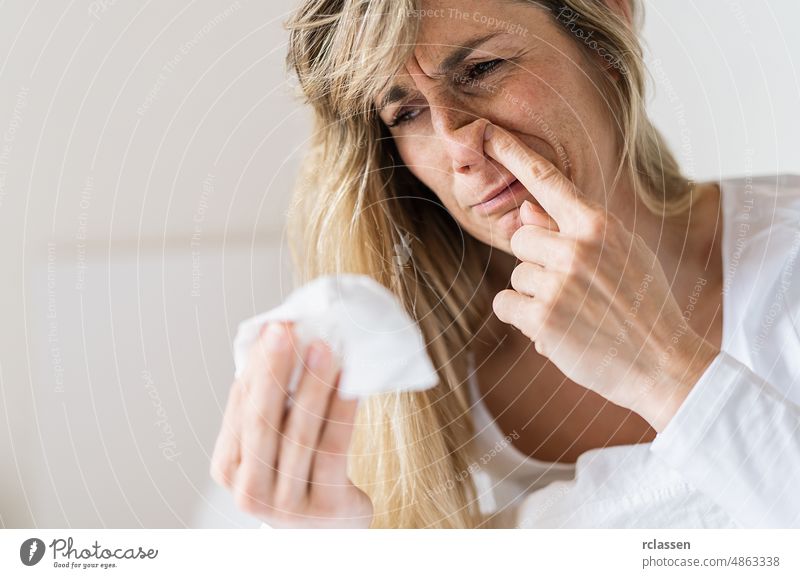 Sick woman Picking his nose. Upset ill european lady sits  in bed, blowing and picks her nose using paper napkin tissue. Cold And Flu Concept allergy bad